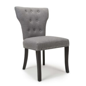 A modern gray upholstered chair with a tufted backrest, silver nailhead trim, and dark wooden legs. The design is elegant and contemporary.